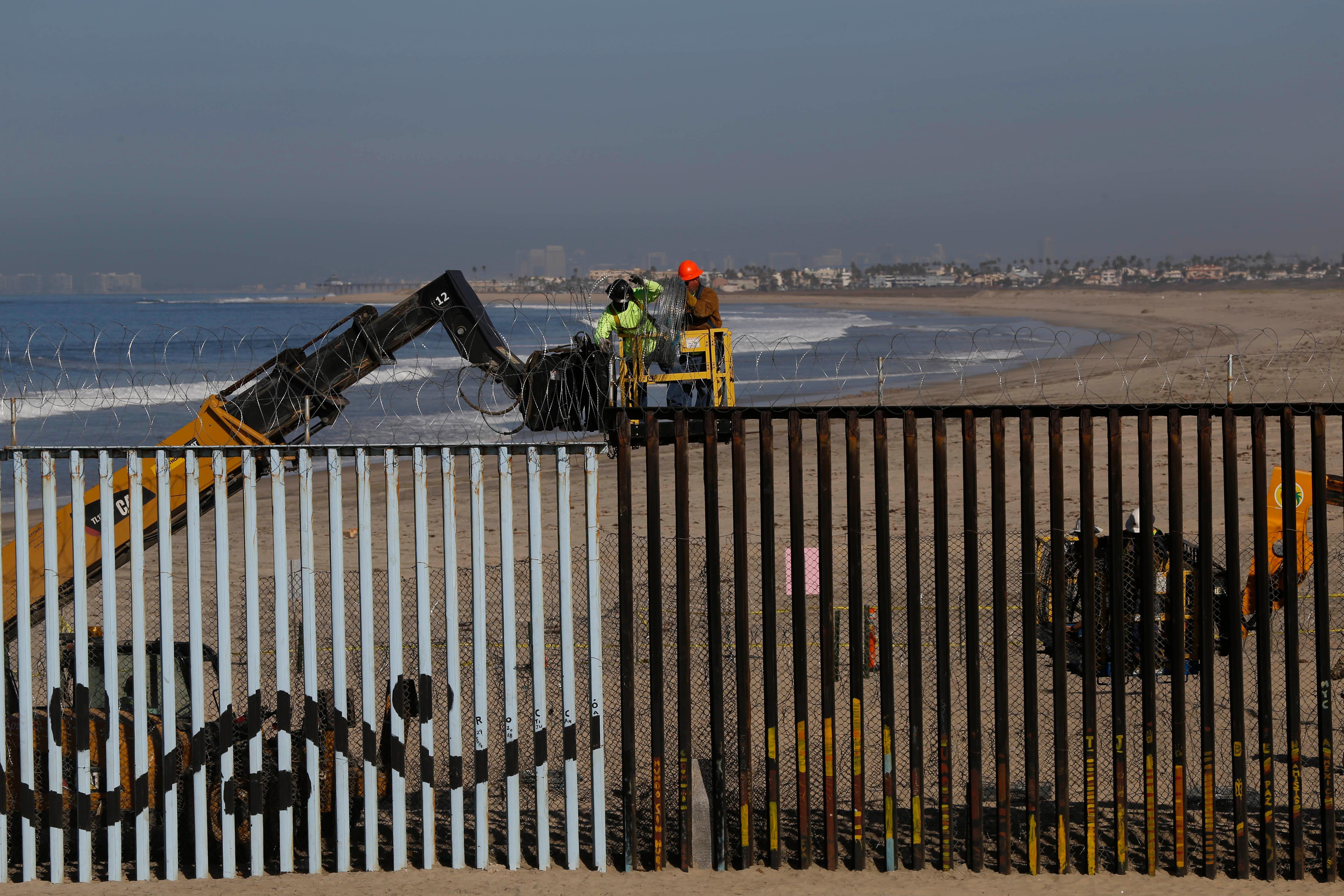 Workers place concertina wire on the border structure Separating Mexico and the United States, where